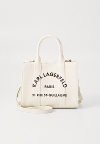 Mała kremowa torba płócienna z dwoma uchwytami i odpinanym paskiem, z czarnym napisem "Karl Lagerfeld Paris 21 Rue St-Guillaume".