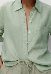 Lichtgroen linnen overhemd met knoopsluiting aan de voorkant, een zakje op de linkerborst en een casual pasvorm, gecombineerd met bijpassende lichtgroene broek.