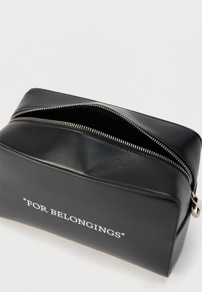 Μαύρο δερμάτινο φερμουάρ με λευκό κείμενο "FOR BELONGINGS" τυπωμένο στο μπροστινό μέρος, εμφανίζεται μερικώς ανοιχτό σε λευκό φόντο.