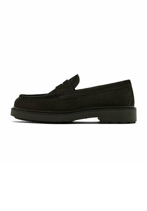 Mocassin en suede noir avec un bout arrondi, des coutures minimales et une semelle en caoutchouc présentant un motif de texture.