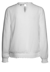 Vit långärmad blus med ett nyckelhål i ryggen, smockad midja och texturerad tyg. Har samlade ärmar vid manschetterna.