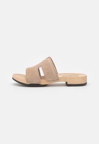 Beige suède schuif sandaal met brede voorkeursband met uitsnijdingen, houten zool en lage blokhak met zwarte rubberen outsole.