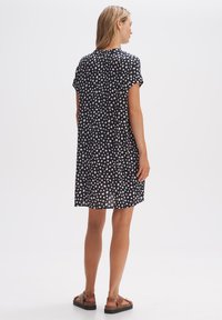 Kurzes ärmelloses navy Kleid mit weißen und rosa Punkten, lockere Passform, knielang, leichtes Material und runder Ausschnitt, getragen mit Sandalen.