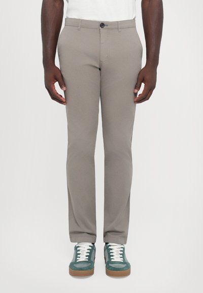 Ανοιχτό μπεζ παντελόνι με στενή γραμμή, λεία υφή, μπροστινές τσέπες και κλείσιμο με έναν κουμπί. Συνδυασμένο με πράσινα και λευκά sneakers.