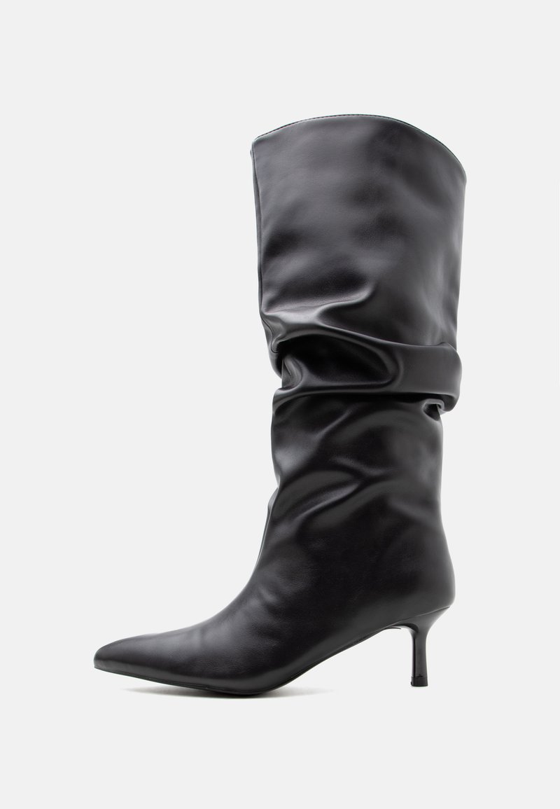 Botte en cuir noire mi-mollet avec bout pointu et talon fin, présentant un design relâché autour de la cheville.