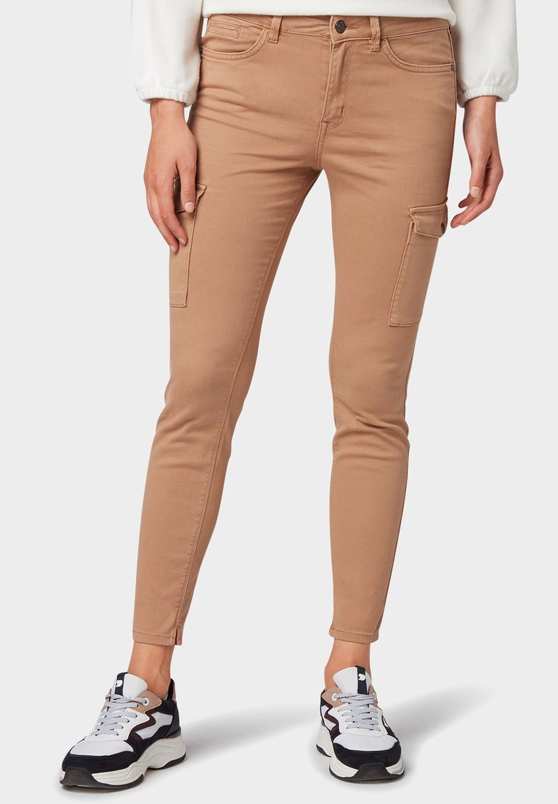 Pantalones cargo color caqui con un corte ajustado, que presentan bolsillos laterales y costuras decorativas. Combinados con zapatillas deportivas en blanco y negro.