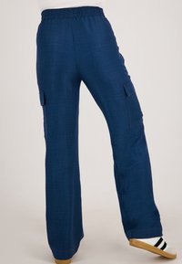 Donkerblauwe, wijde broek van textuurstof met een elastische tailleband en zijzakken voor extra functionaliteit.