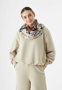 Ensemble composé d'un sweat beige et d'un pantalon, agrémenté d'une écharpe à motifs multicolores, présentant des nuances de marron, de gris et de noir dans un design en boucle.
