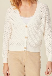 White knitted cardigan with a diamond pattern, featuring a V-neck, long sleeves, and wooden buttons. Ribbed cuffs and hem.