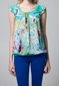 Blouse sans manches, légère, avec des épaules froncées dans des motifs abstraits bleus et verts, associée à un pantalon ajusté bleu.