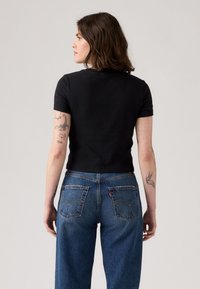 T-shirt noir court à manches courtes, associé à un jean en denim bleu taille haute avec deux poches arrière et un détail de couture.