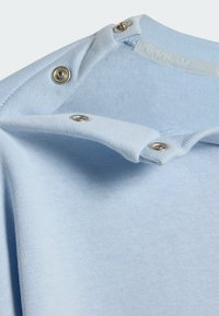 Svijetloplava pamučna košulja s kopčama na ovratniku. Glatka tekstura, kratki rukavi i zaobljeni izrez oko vrata.