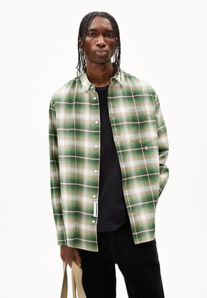 Groen en witte geruite shirt met een knoopsluiting, voorzien van lange mouwen en een borstzak. Draagt over een zwart T-shirt.