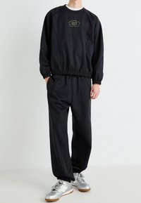 Czarny sportowy dres składający się z bluzy z okrągłym dekoltem, elastycznymi mankietami i spodni ze sznurkiem. Do kompletu srebrne sneakersy.