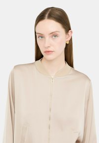 Giacca bomber in satin beige con chiusura a zip, colletto a coste e tasche laterali. Dettagli in hardware dorato aggiungono un tocco di stile.