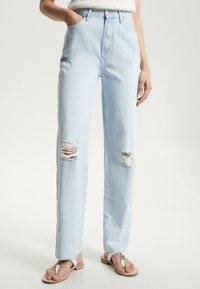 Jeans de tiro alto en un azul claro, hechos de denim, con dos desgastes en la parte delantera, diseño de pierna recta y un desgaste sutil en el dobladillo.