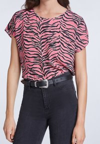 Haut à manches courtes à imprimé zèbre rose, tissu léger, encolure ronde, associé à un jean noir taille haute et une ceinture noire avec une boucle argentée.