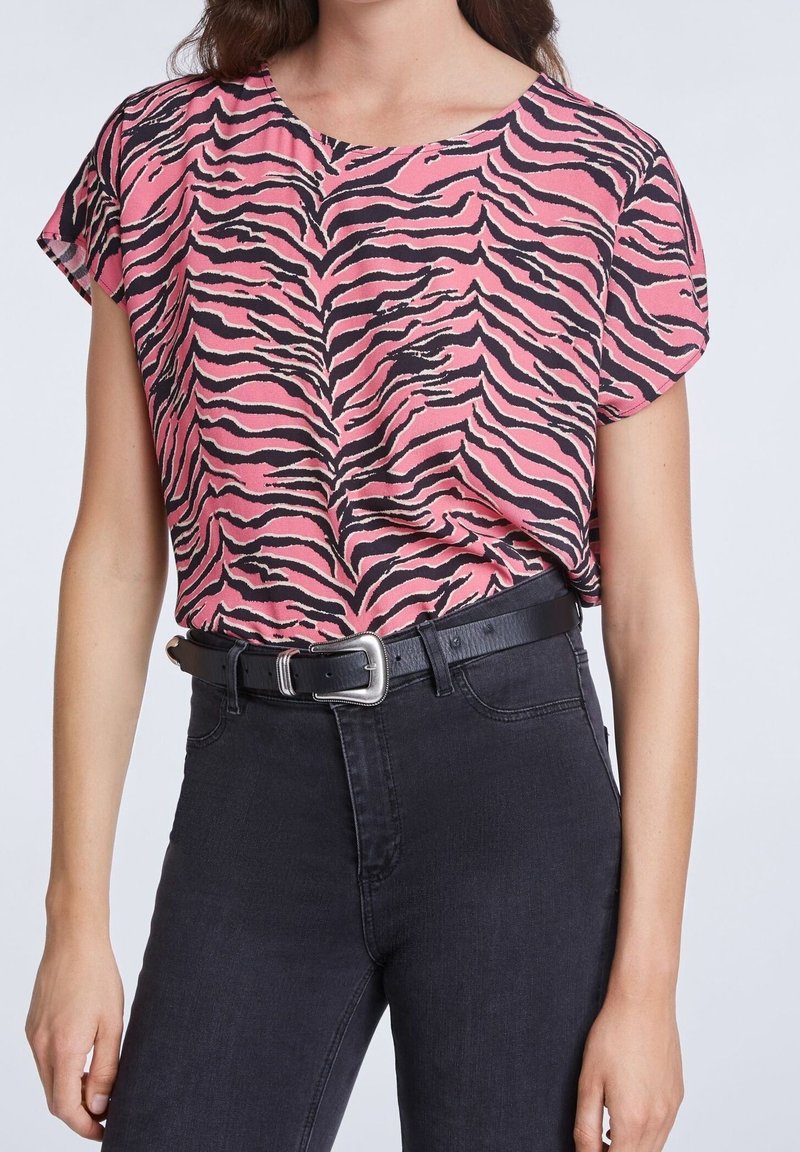 Haut à manches courtes à imprimé zèbre rose, tissu léger, encolure ronde, associé à un jean noir taille haute et une ceinture noire avec une boucle argentée.