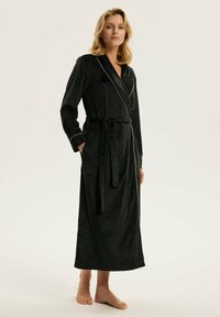 Czarna szata z miękkiego materiału, z fasonem nawiązującym do owijania, długimi rękawami i paskiem w talii z różowymi akcentami.