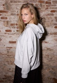 Szara bluza z kapturem o luźnym kroju, z prążkowanymi mankietami i teksturowanym wzorem z przodu, zestawiona z ciemną, paskowaną spódnicą.