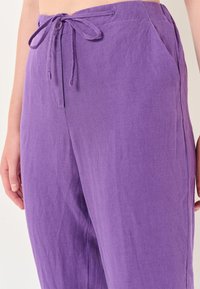 Paarse linnen broek met een tailleband met trekkoord, zijzakken en een relaxte pasvorm. De stof heeft een gestructureerde, licht gekreukte uitstraling.