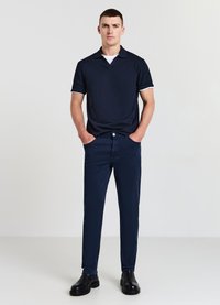 Navyblaues Poloshirt mit weißem Kragenbesatz, kombiniert mit navyblauen Slim-Fit-Hosen und schwarzen Schuhen, minimalistisches Design, glatte Stofftextur.