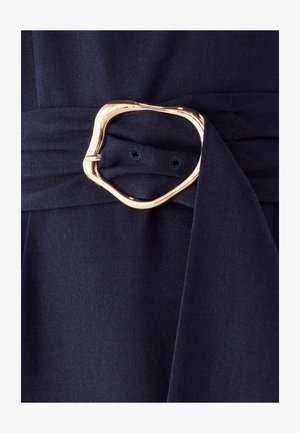 Navy blue fabric with a smooth texture, featuring a large, abstract gold metal buckle on a tied waist detail.