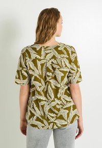 Chemise à manches courtes vert olive avec un motif de feuilles blanches, col rond, coupe décontractée et finition en tissu texturé.