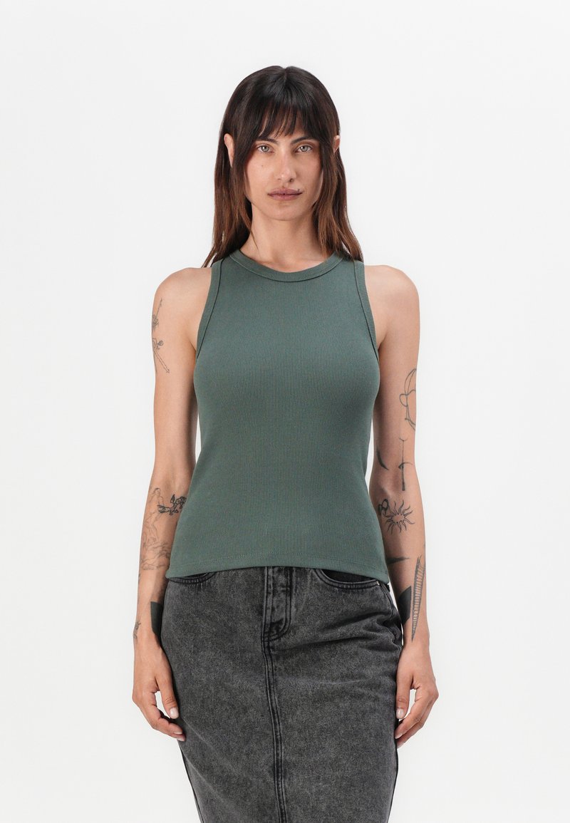 Grønn ribbestrikket tanktopp med høy hals, tettsittende design og ermeløs snitt, kombinert med et svart denimbunn for kontrast.