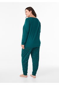 Türkisfarbenes Lounge-Set bestehend aus einem langärmligen Oberteil und gemusterten Hosen. Das Oberteil ist einfarbig, während die Hosen mit einem Blumenmuster versehen sind.