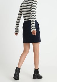 Marinblå kordkjol i mini-längd med sidofickor, ihop med en randig långärmad tröja. Svarta ankelskor med klumpig klack.