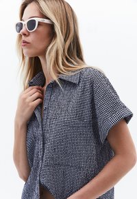 Kortärmad, rutigt skjorta i marinblått och vitt bomull med krage. Bärs med vita solglasögon med ett stilrent, minimalistiskt design.