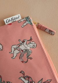 Rožinė užtrauktuko kišenėlė, kurioje yra pasikartojanti chervų ir juostelių raštas. Pagaminta iš tekstūruoto audinio, turi auksinį užtrauktuką ir audinio rankenėlę.