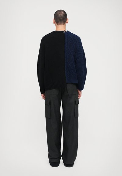 Knit sweater featuring a split design in black and dark blue, textured patterns, with dropped shoulders, paired with loose black cargo pants.