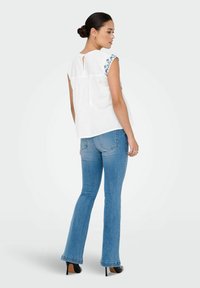 Hvid bluse med broderede blå blomsterdetaljer på skuldrene, ryggens nøglehulldetalje, parret med lysvaskede flared jeans og sorte hæle.
