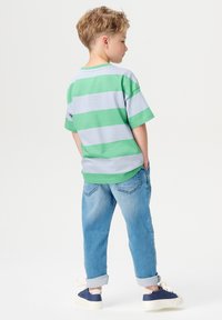 Gestreiftes T-Shirt in Grün und Hellgrau, mit kurzen Ärmeln, kombiniert mit hellblauen hochgekrempelten Jeans und marineblauen Sneakers; von hinten gesehen.