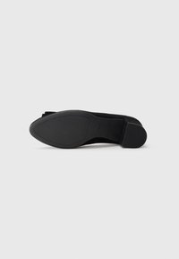 Scarpa nera in suede con tacco alto, punta rotonda e suola in pelle texturizzata. Presenta un tacco a blocco modesto per maggiore stabilità.