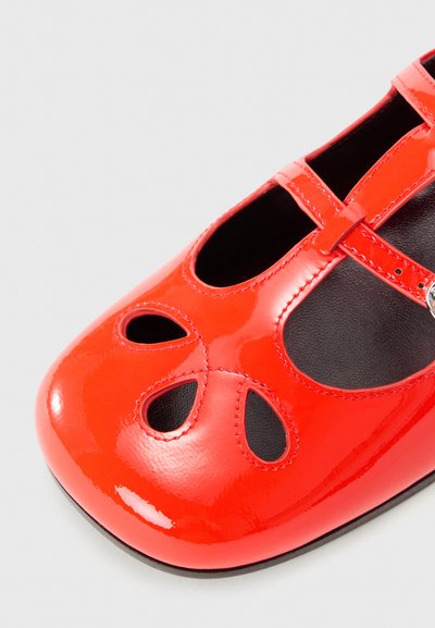 Red patent leather ballet flats featuring a rounded toe, cut-out details, and adjustable strap for secure fit. Black interior lining.