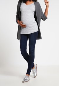 Grå stickad cardigan över en grå v-ringad topp, tillsammans med mörkblå jeans och glänsande silverfärgade skor. Utrustningen har en avslappnad passform.