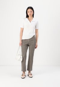 Polo shirt blanc à manches courtes, pantalon à carreaux marron et noir, sac à main blanc et mocassins beiges avec des sangles. Design minimaliste et coupe ajustée.