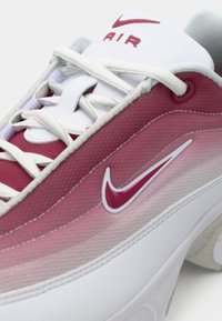 Červené a biele športové tenisky s hladkým syntetickým materiálom, textúrovaným gradientným dizajnom, výrazným logom Nike a bielymi šnúrkami.