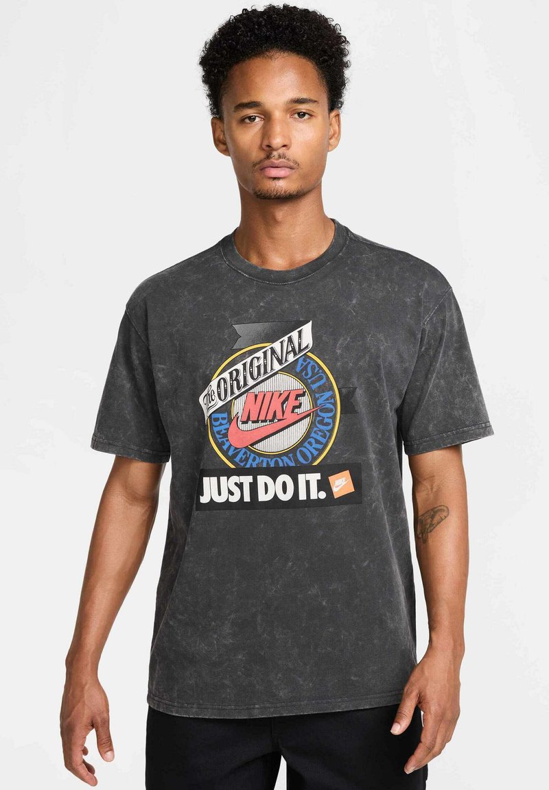 T-shirt in cotone nero con grafica Nike in stile vintage, logo circolare e slogan "JUST DO IT." Maniche corte e vestibilità rilassata.
