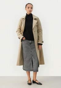 Beige Trenchcoat über einem schwarzen Rippstrickpullover, kombiniert mit einem grauen Jeansrock mit Schlitz vorne und schwarzen Ballerinas.