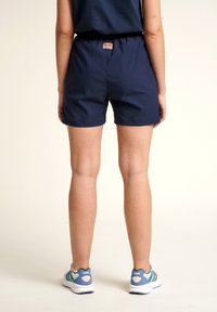 Marineblaue Shorts mit einem elastischen Bund, mit einem kleinen Logo-Patch auf der Rückseite. Kombiniert mit weißen und blauen Sport Schuhen.