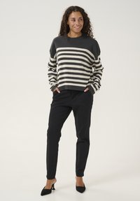 Gestreifter Pullover in Dunkelgrau und Creme, mit Rundhalsausschnitt und weiten Ärmeln. Kombiniert mit schwarzen, schmal zulaufenden Hosen und schwarzen Absätzen.