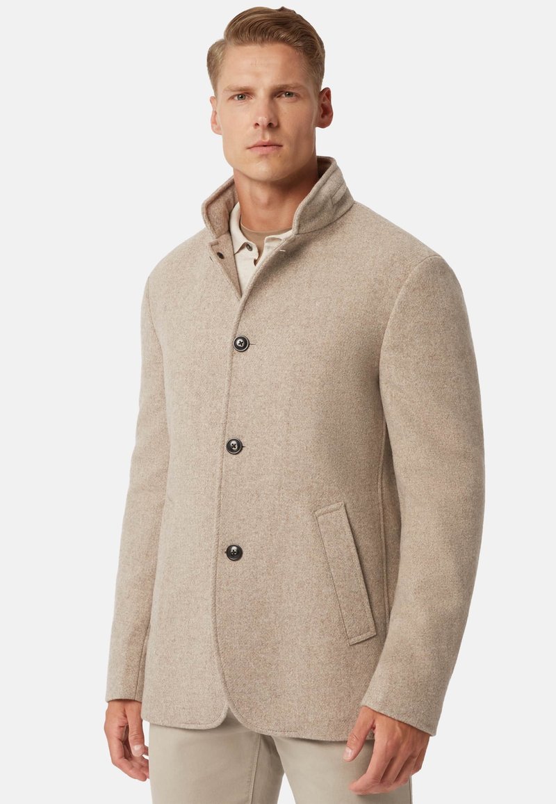 Abrigo de mezcla de lana beige con cuello alto, cinco botones negros, un bolsillo y un corte entallado. Textura suave y diseño estructurado.