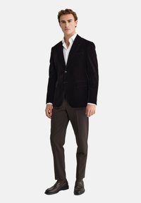 Melnā zīda žakete ar šķērsgriezumu, vienu pogu un divām priekšējām kabatām. Valkāta virs baltas kreklu un apvienota ar brūniem biksēm un mokasīniem.