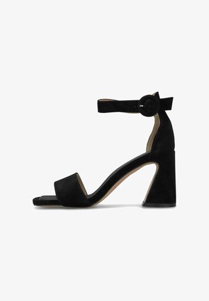 Schwarze Wildleder-High-Heel-Sandale mit Knöchelriemen und runder Schnalle, offen an der Spitze und Blockabsatz, von der Seite vor einem weißen Hintergrund gezeigt.