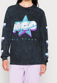 Černé tričko s dlouhým rukávem s texturovaným povrchem, které má velký vícolorový grafický design hvězdy a menší grafiky na rukávech.