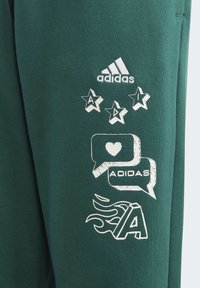 Sudadera verde con gráficos impresos en blanco: logo de Adidas, estrellas, burbujas de diálogo con corazones y llamas estilizadas. Material de mezcla de algodón.